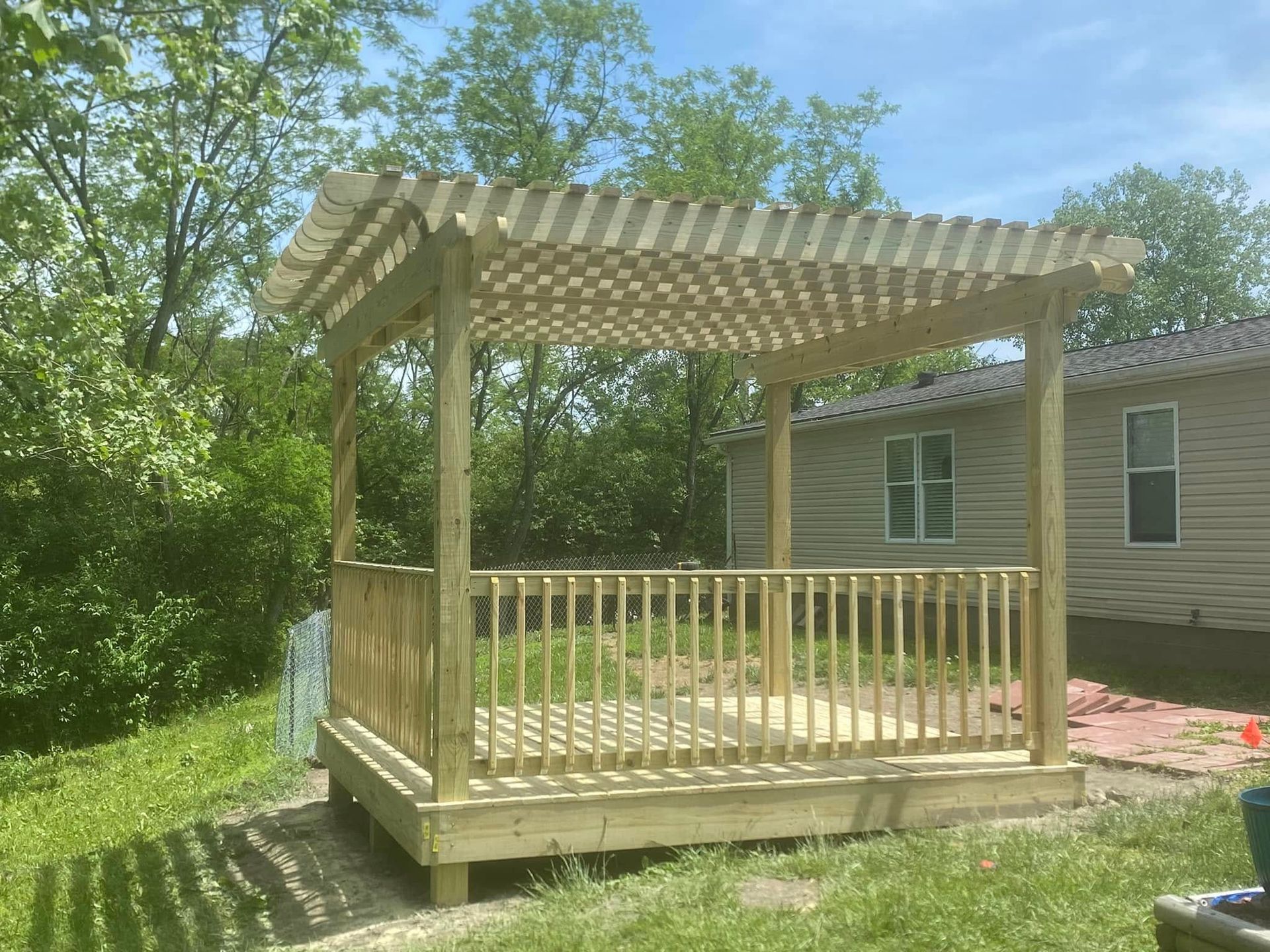 A wooden deck with a pergola and railing in front of a house.