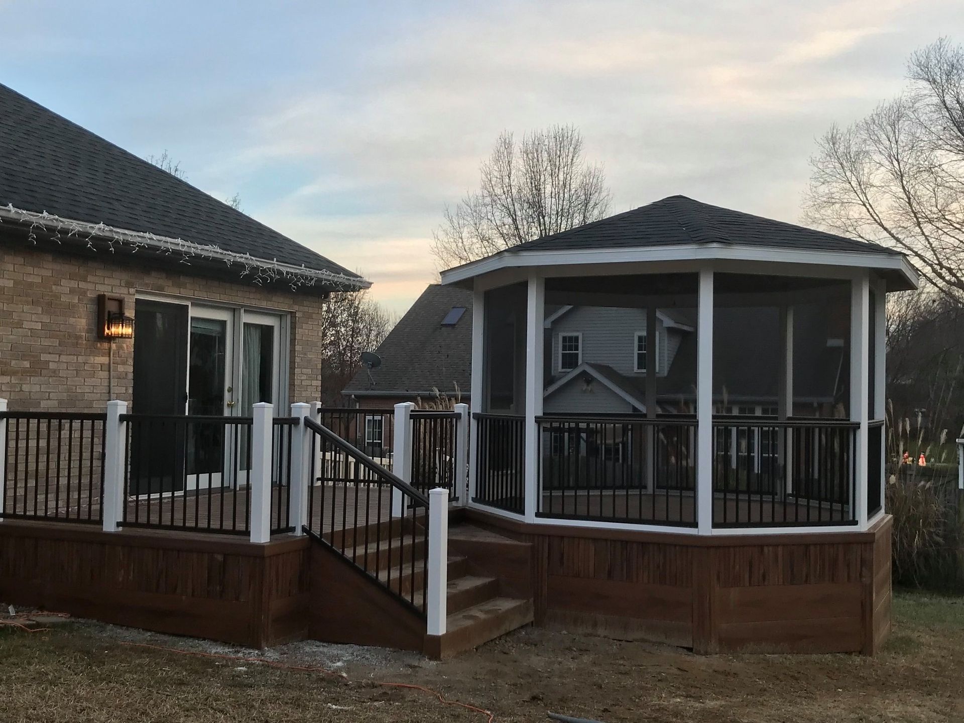 A screened in gazebo on a deck next to a house.