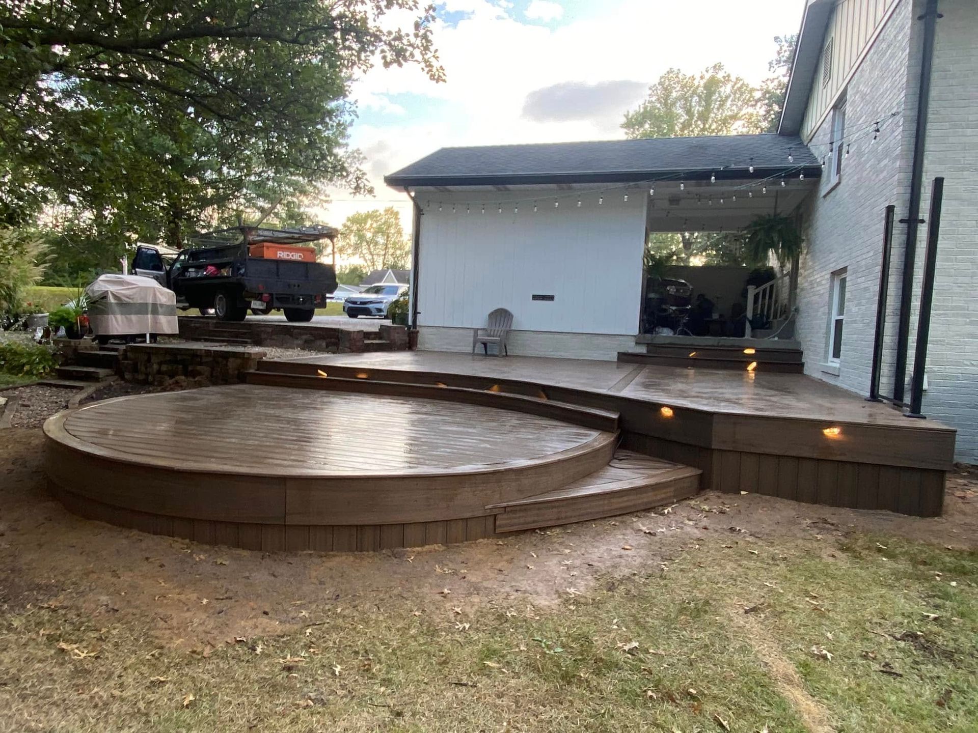 A large circular deck with stairs leading up to it is in front of a house.