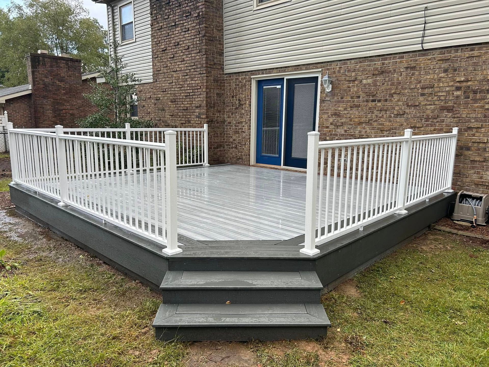 A large deck with stairs and a white railing in front of a brick house.
