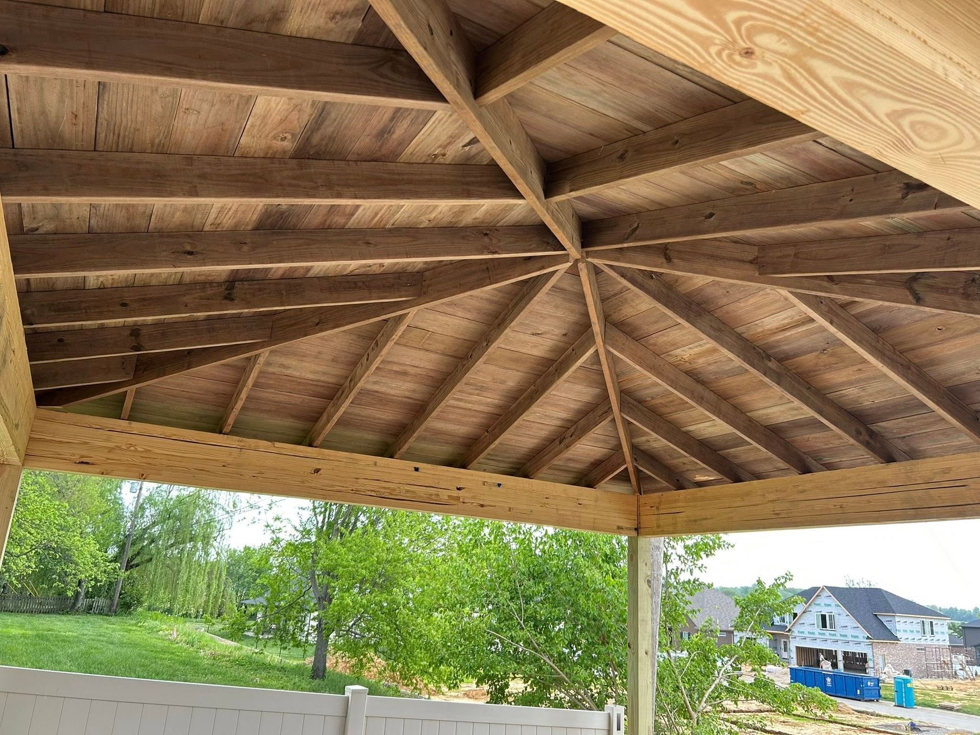 A gazebo with a wooden roof and a white fence