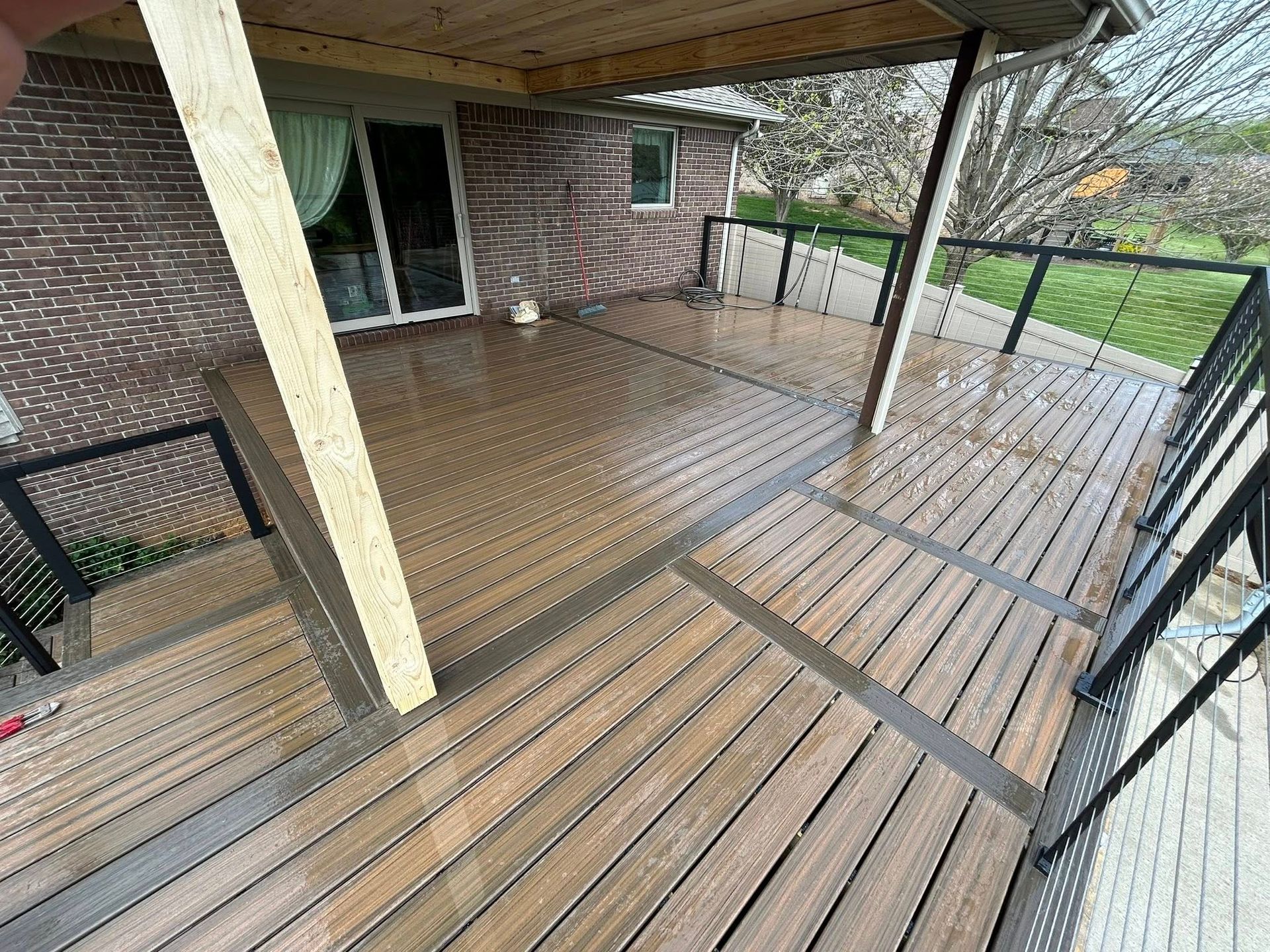 A wooden deck with a railing and a brick house in the background.