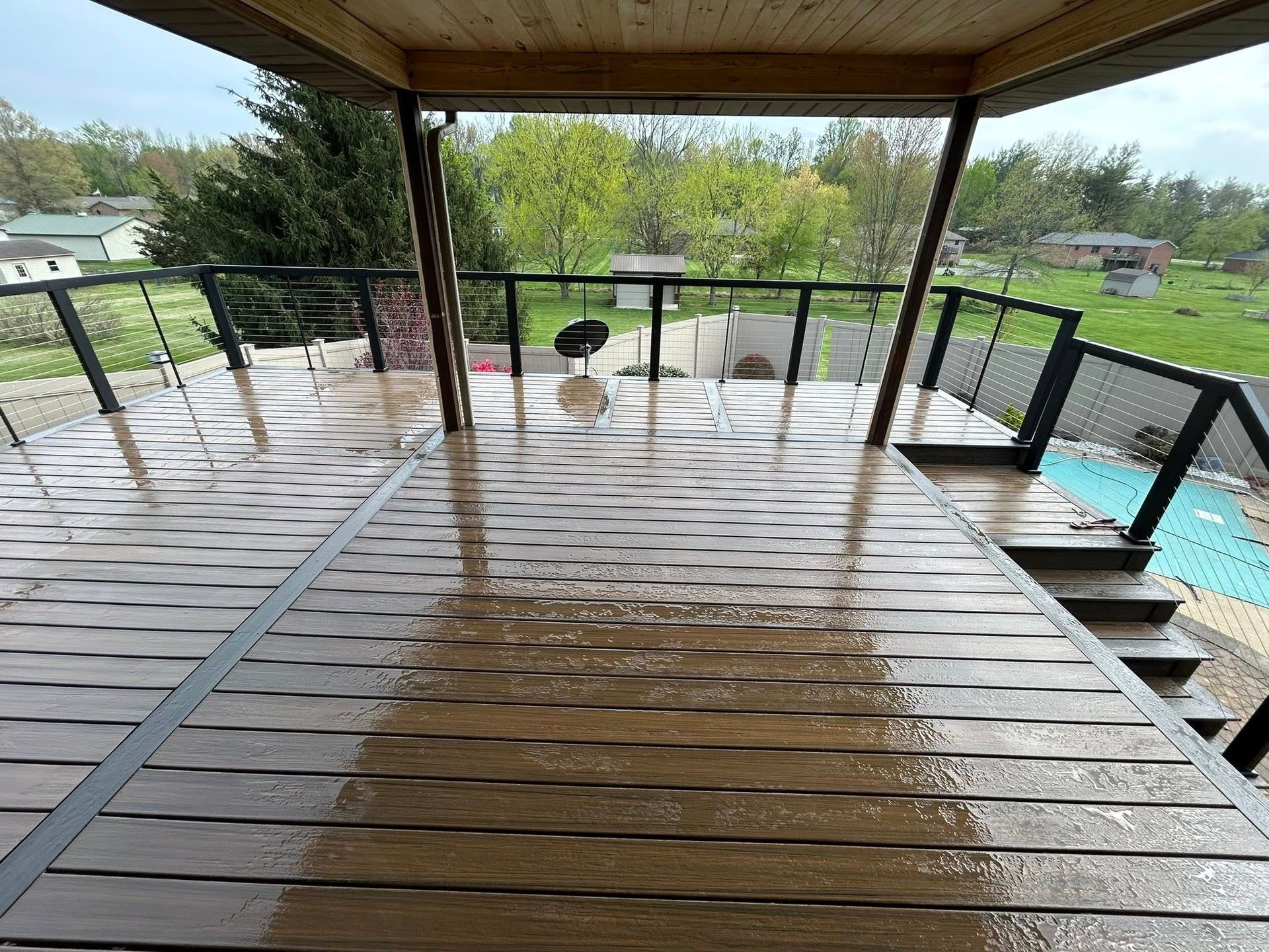 A wooden deck with stairs leading up to it and a view of a lush green field.