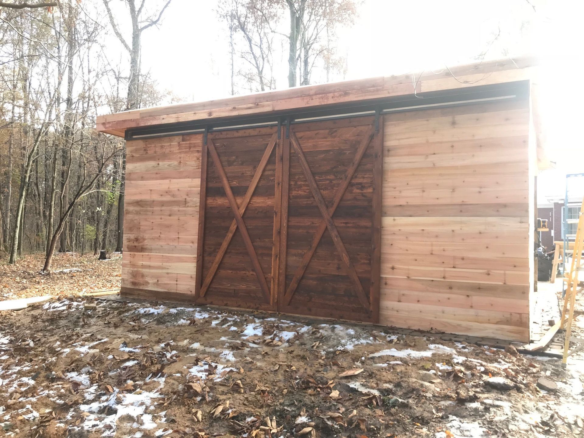 A wooden shed with a sliding barn door is sitting in the middle of a dirt field.