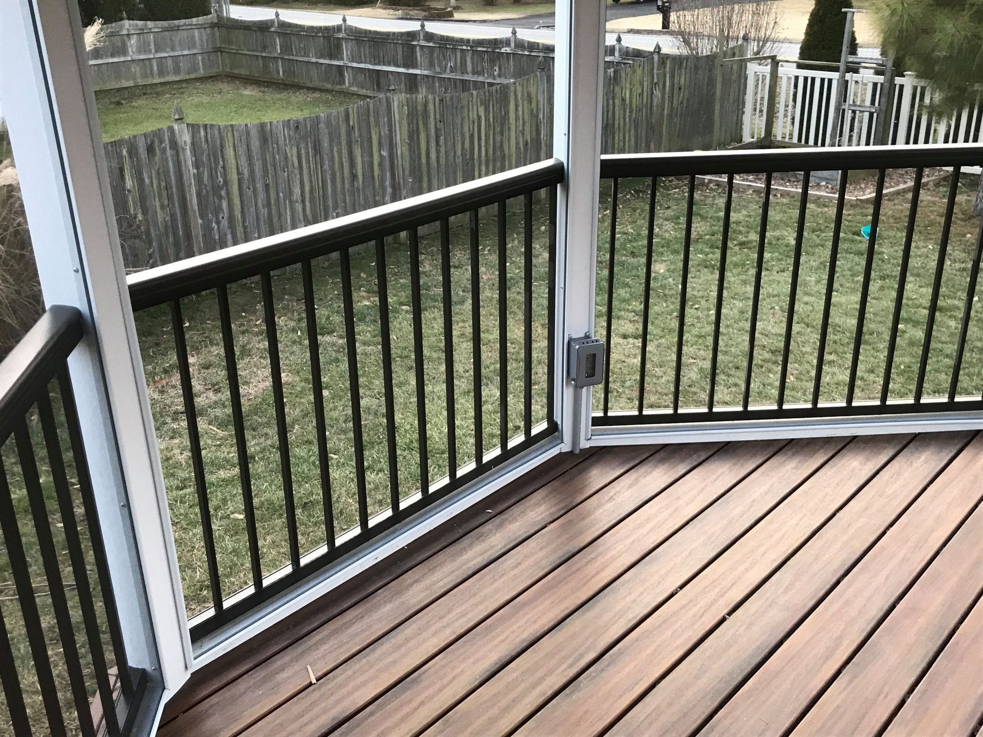A screened in porch with a wooden deck and black railing.