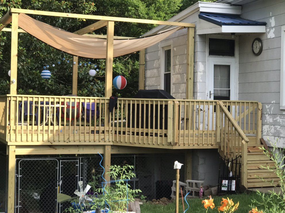 A wooden deck with a canopy over it is in front of a house.