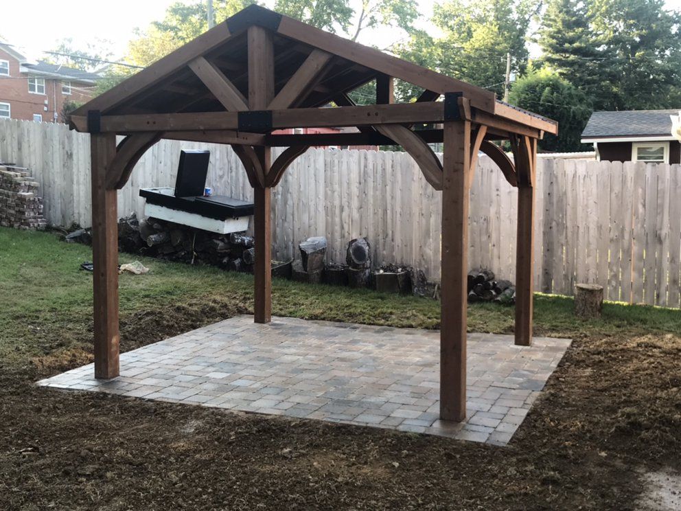 A wooden gazebo is sitting on top of a brick patio in a backyard.