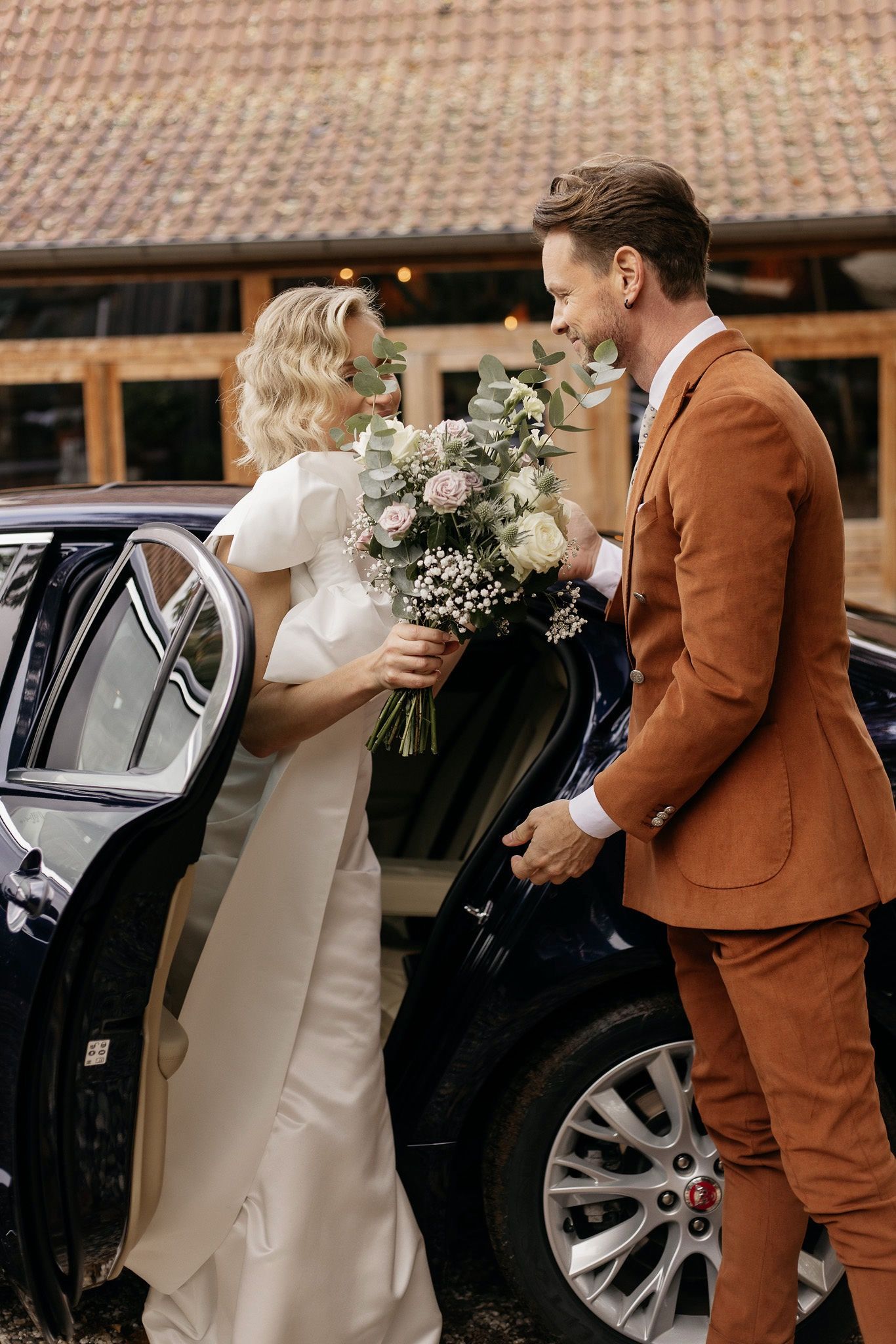 bruidspaar stapt uit bruidsauto met het bruidsboeket 