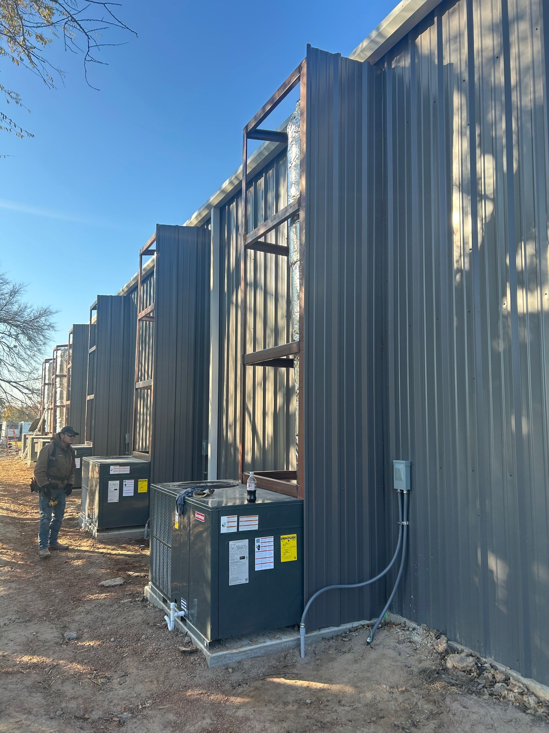 Exterior view of a building with multiple HVAC units along the wall, with a person inspecting them.