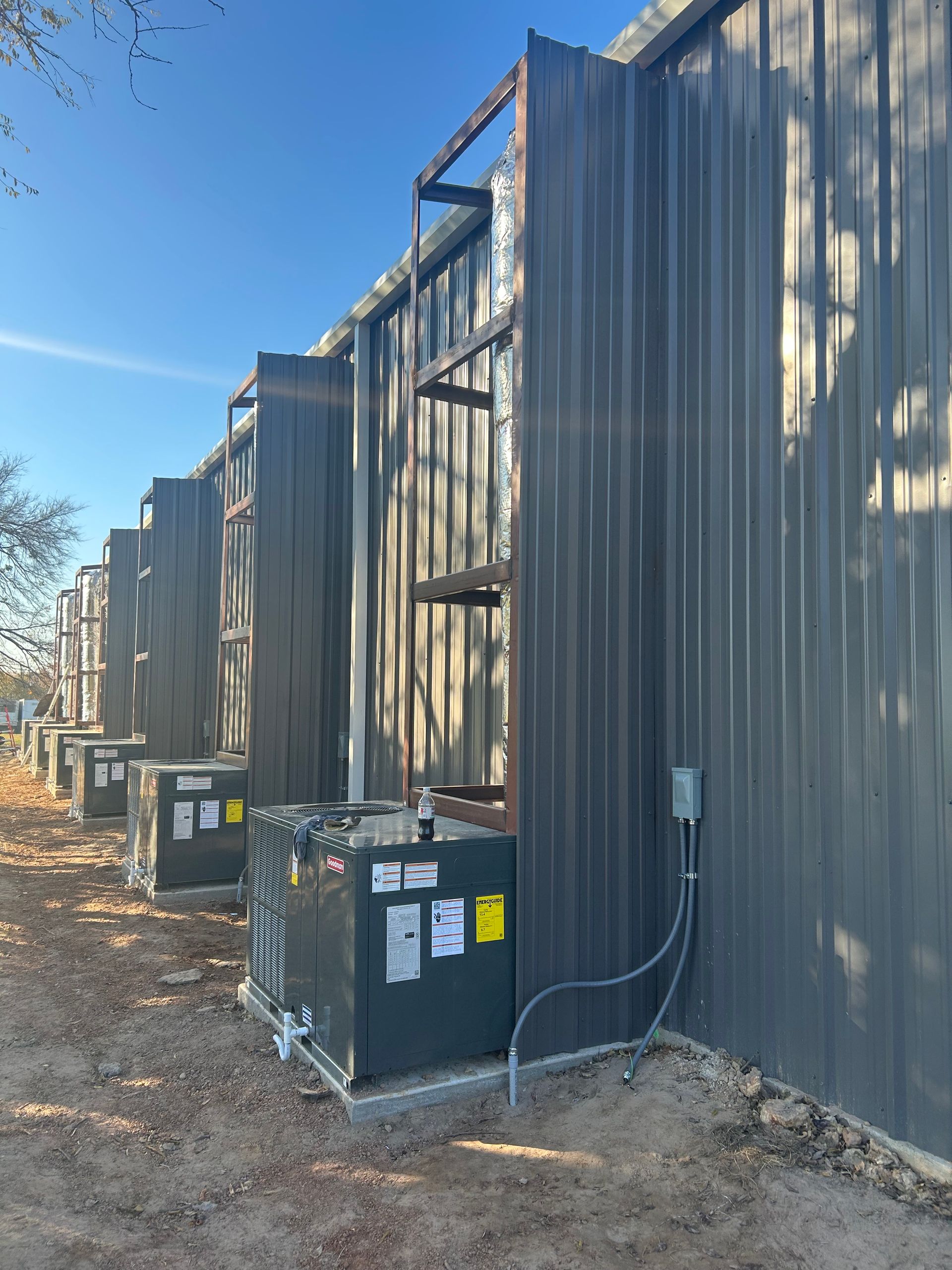 Row of dark metal buildings with HVAC units outside on a sunny day.