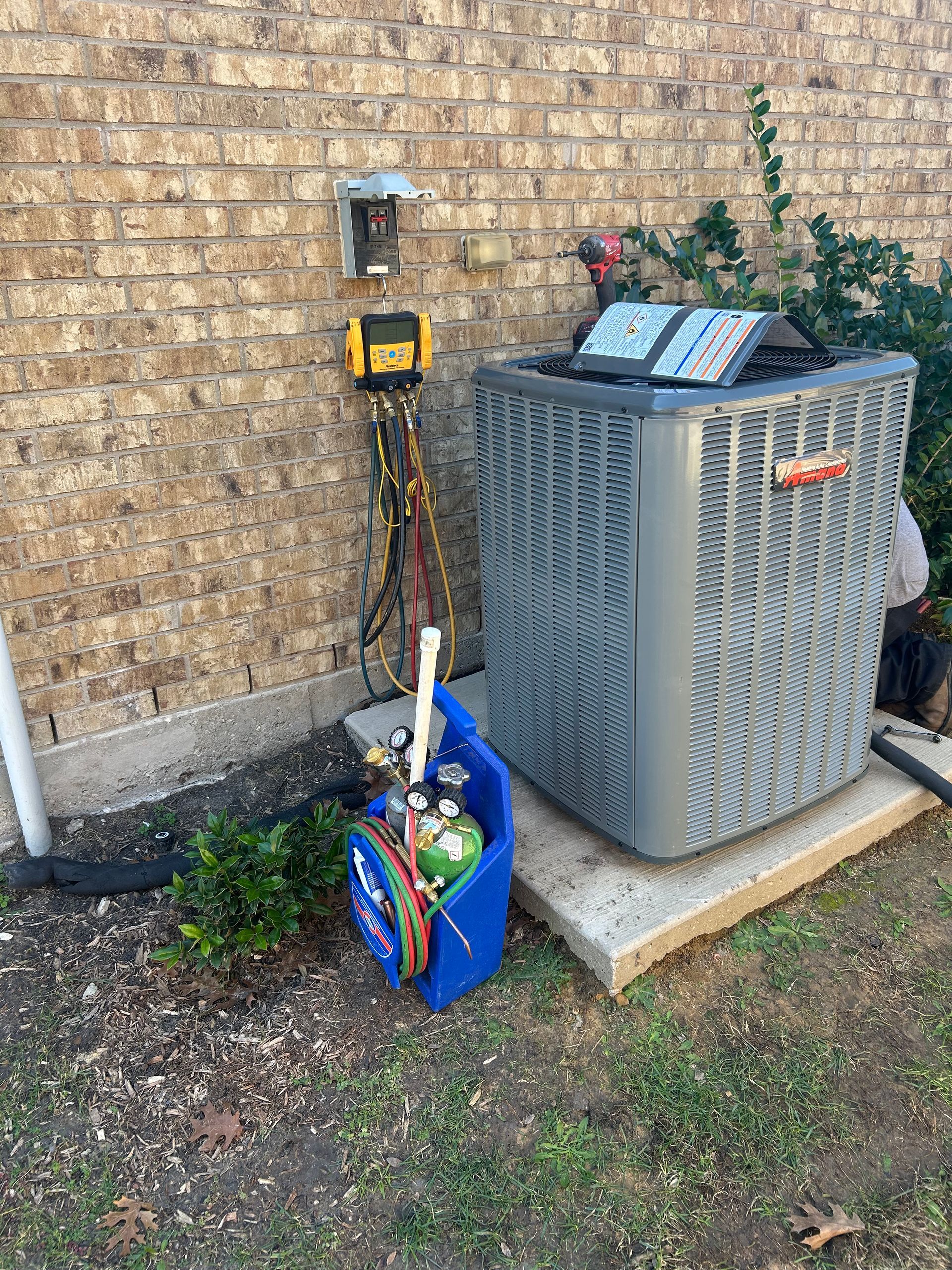 HVAC unit next to a brick wall, with equipment connected for servicing.