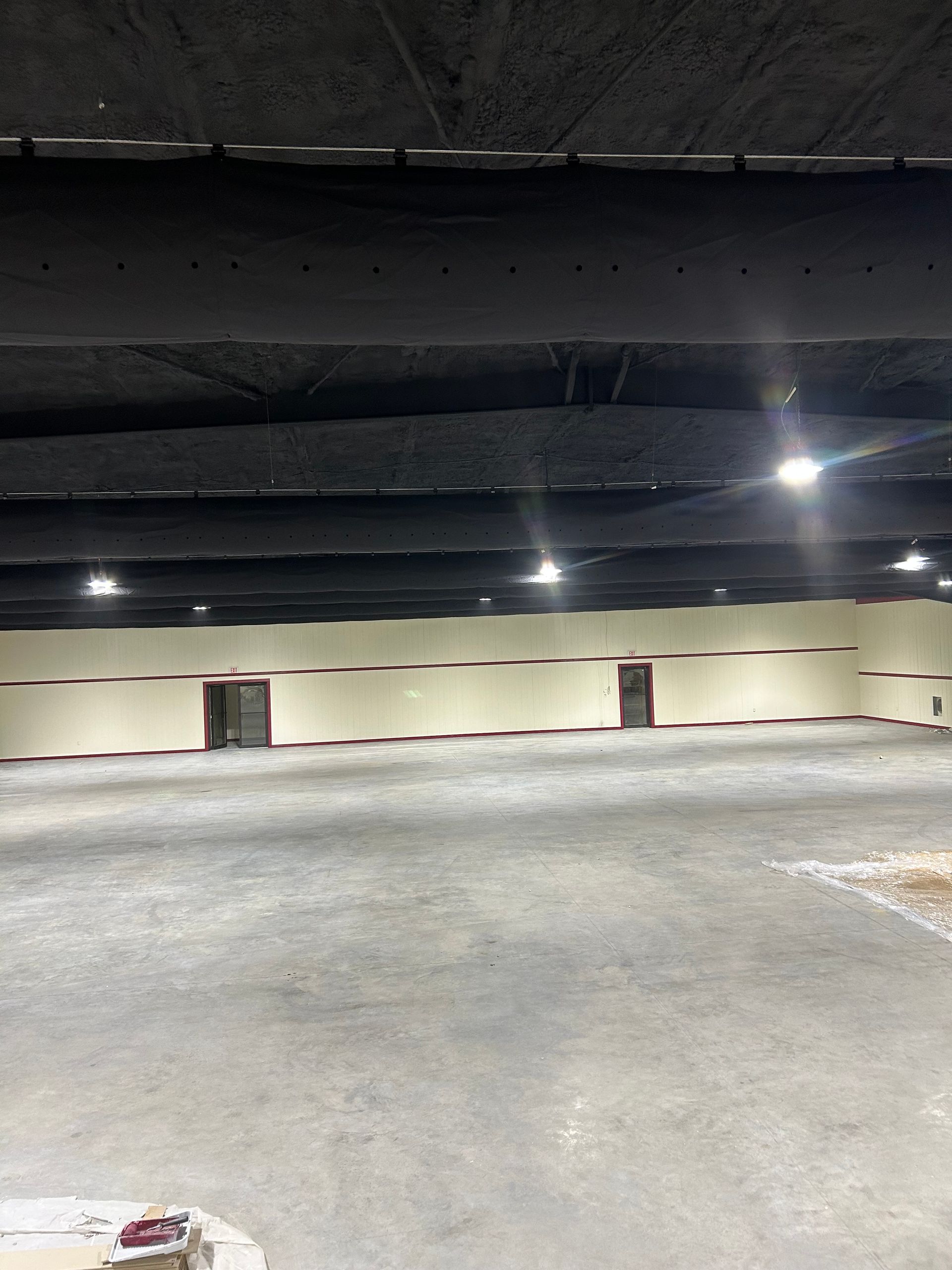 Empty concrete room with a tan wall and doors. Black ceiling with lights.