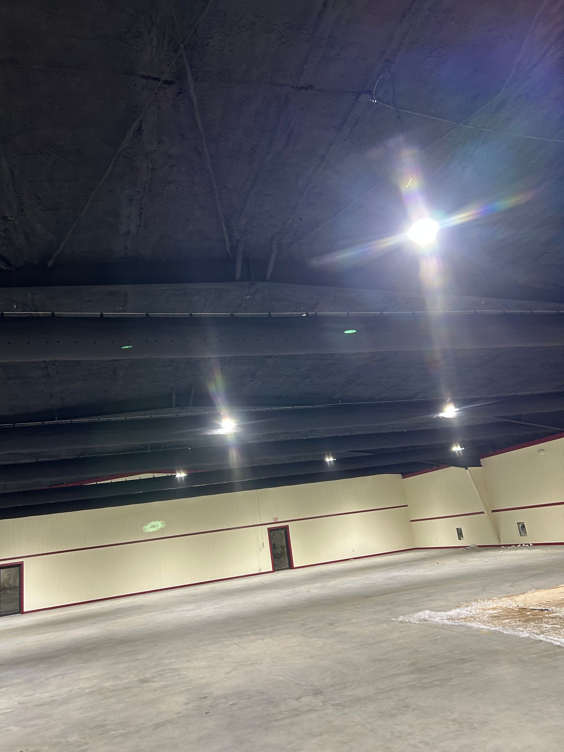 Large empty interior space with high ceiling, bright overhead lights, and light-colored walls.
