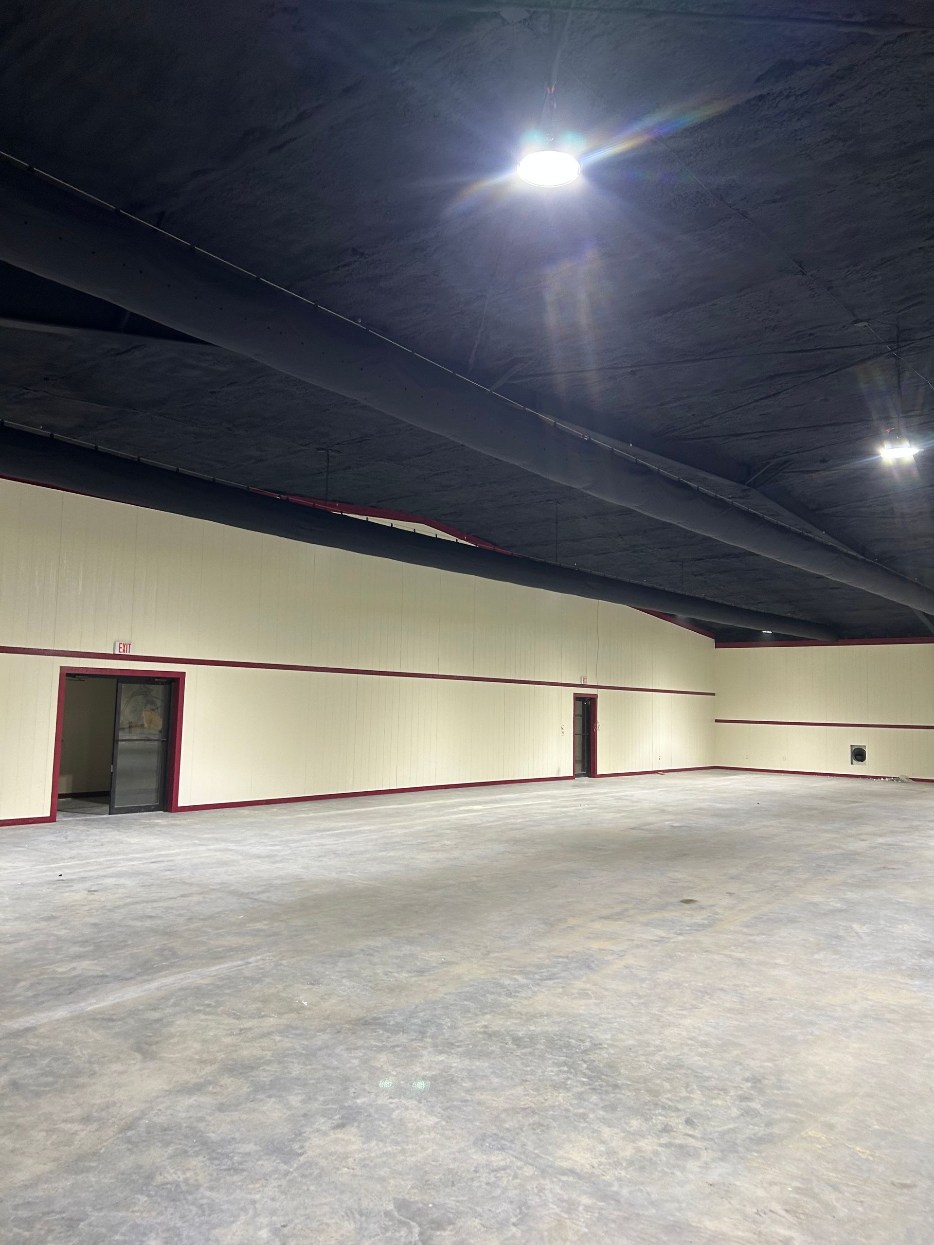 Empty indoor space with concrete floor, tan walls, dark ceiling, and a few doors.