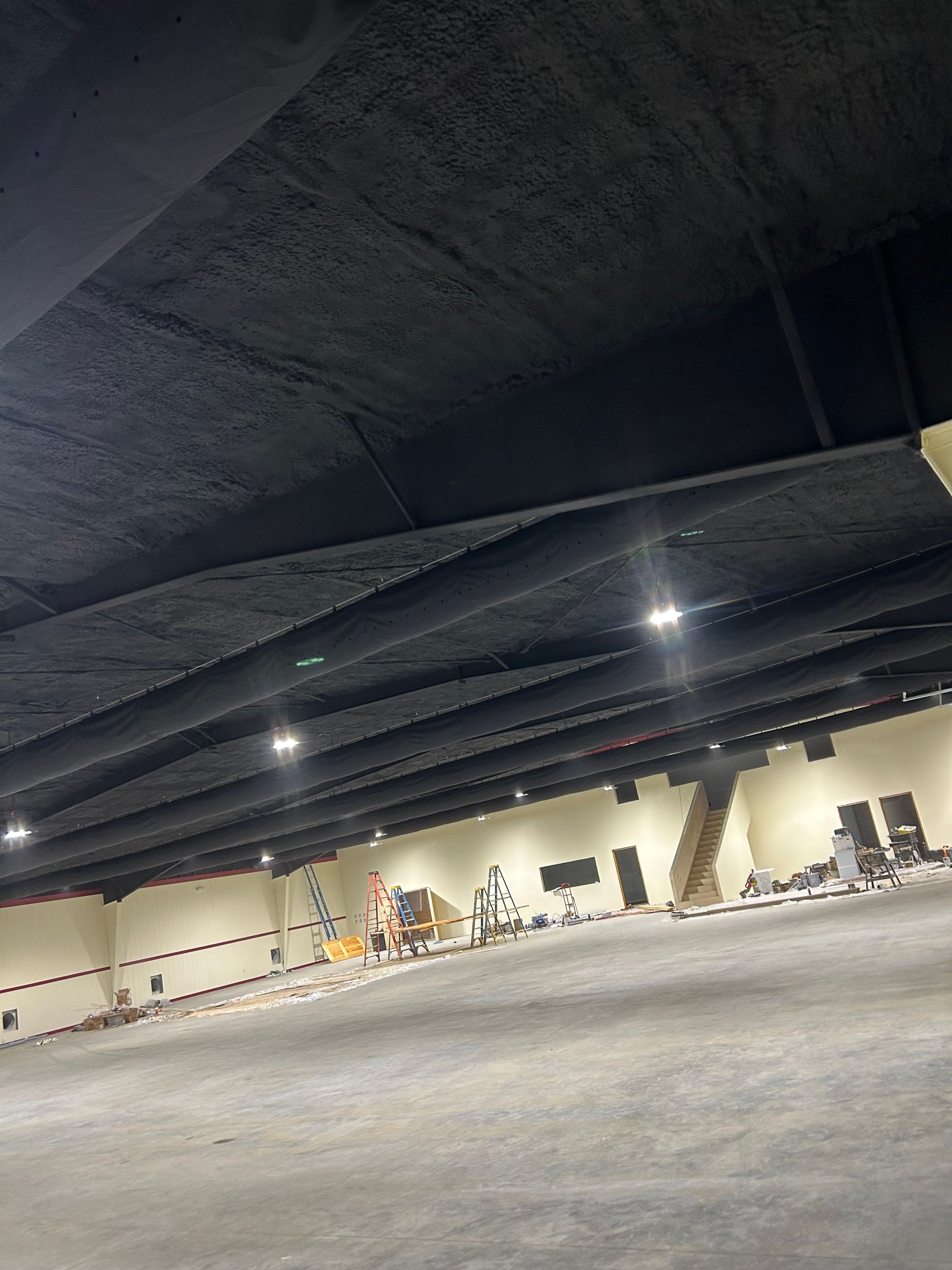 Large, empty commercial space with black ceiling and recessed lights. Beige walls and concrete floor.