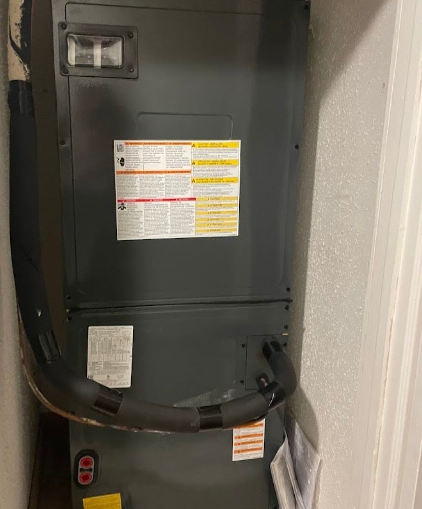HVAC unit in a closet. Gray metal box with warning labels, black insulated tubing, and air vents.