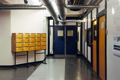 Hallway with mailboxes, blue door, and yellow door. Pipes run overhead.