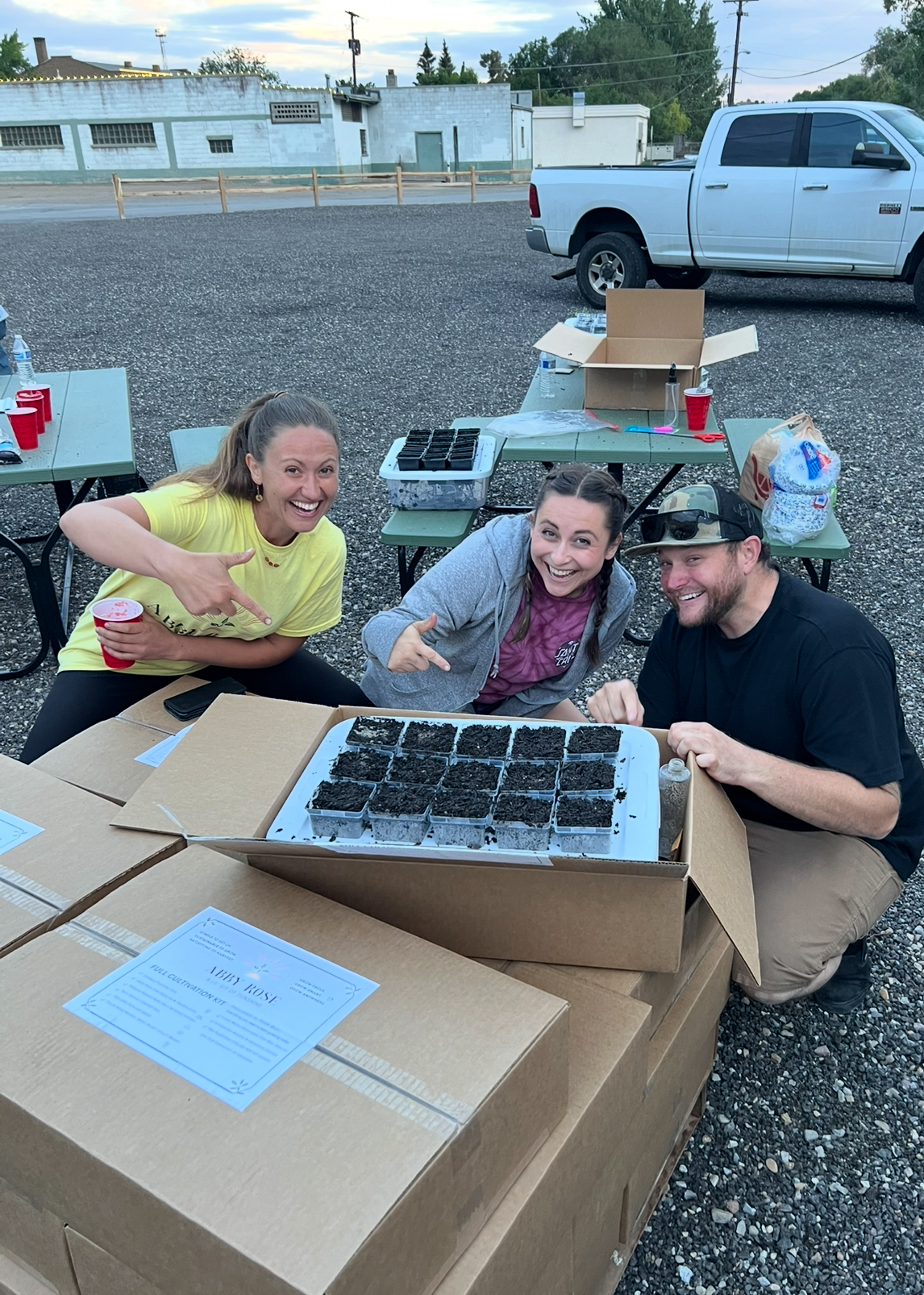 Three people with excited expressions, planting seedlings in an Abby Rose Kit box outdoors.