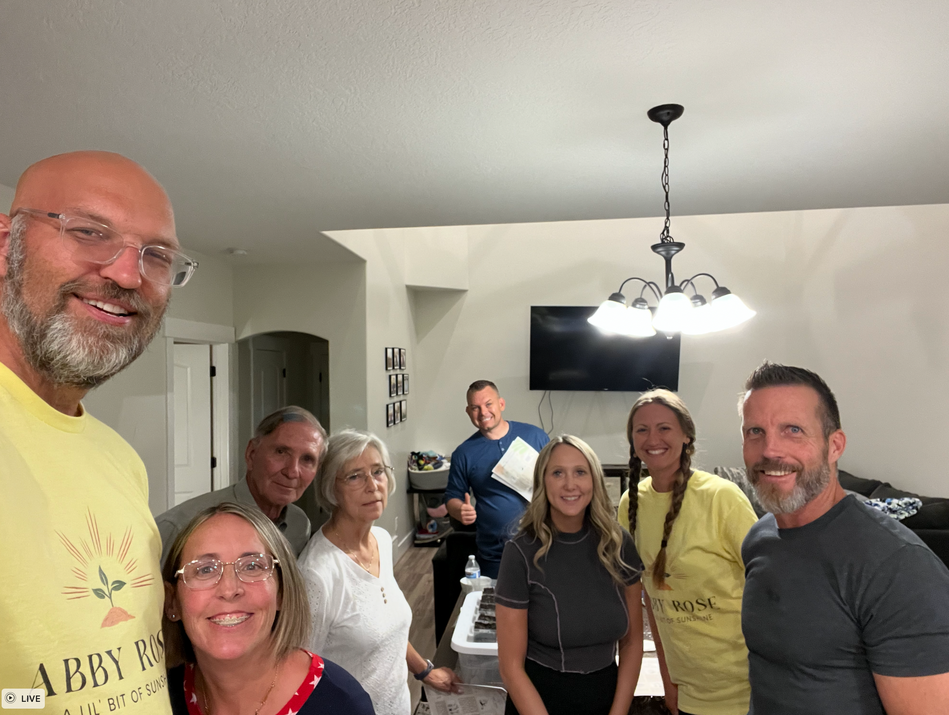 Group of people smiling at the camera in a home. Some are holding papers.