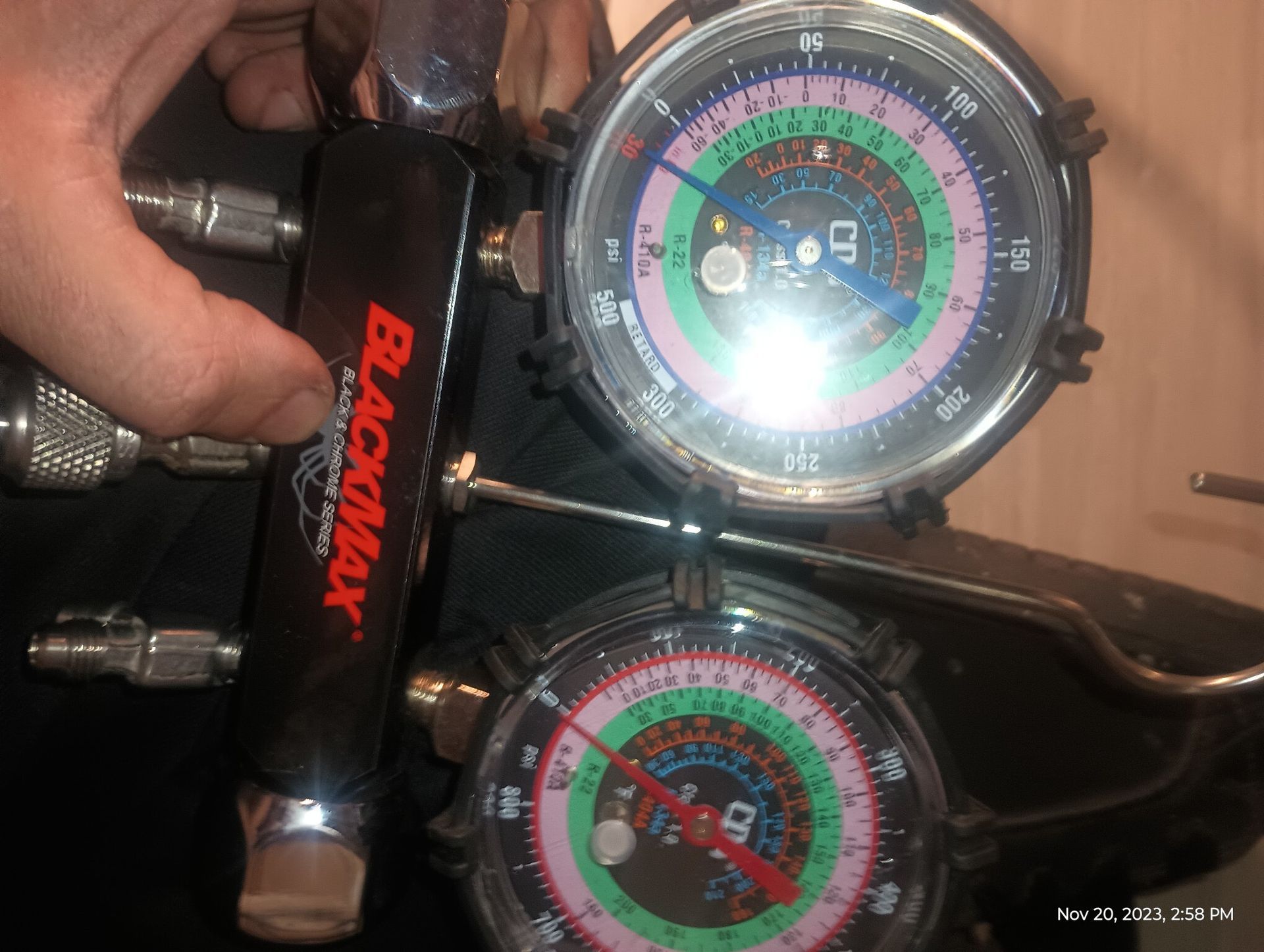 Handheld Black Maxx AC gauges with colorful dials attached to metal fittings, in a workshop setting