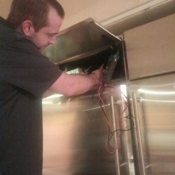 Technician working inside an open stainless steel cabinet, handling exposed wires.