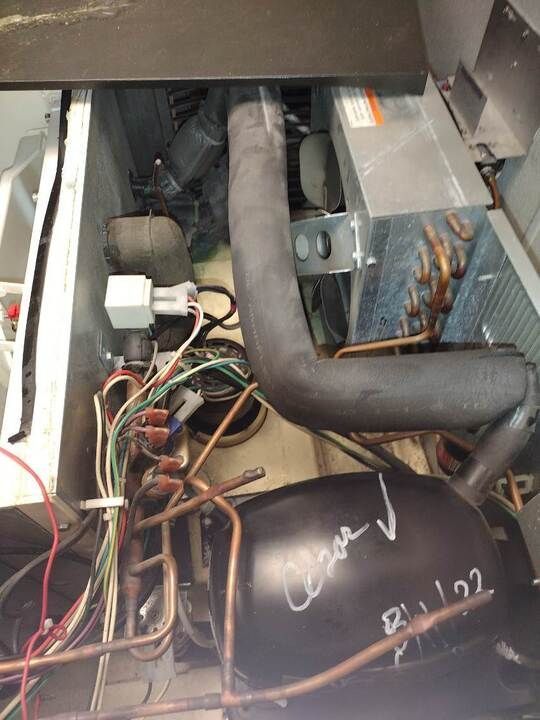 Open HVAC or appliance interior with black ducting, wiring, and metal components inside a cramped compartment.