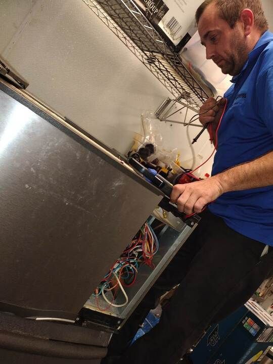 Technician in blue shirt working on an open electronics cabinet with exposed wires in a workshop
