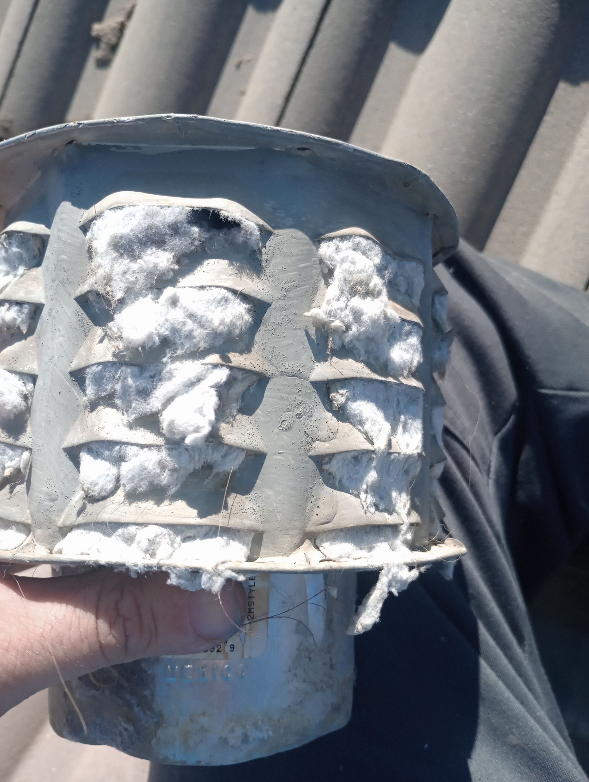 Close-up of a white, soot-covered metal part with a hand holding it outdoors.