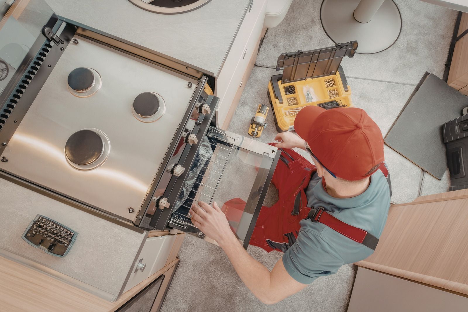 Person in orange cap and red apron working at a metal machine in a workshop, viewed from above