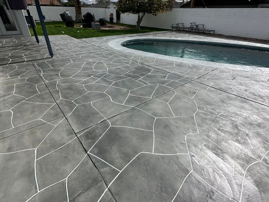 Gray stone-patterned concrete pool deck with visible joints and a curved swimming pool edge.