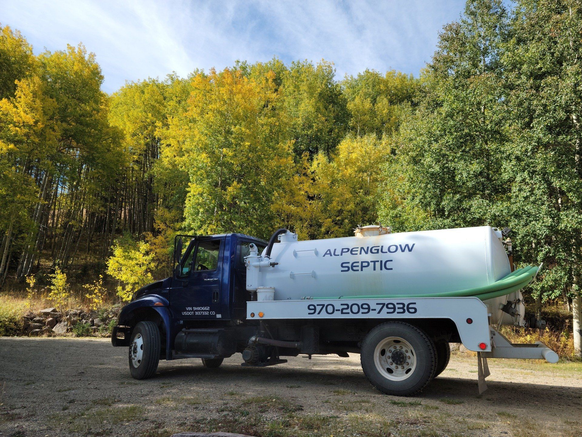 Black truck with white water tank parked by trees in autumn, labeled “Aluminum Septic” with phone number.