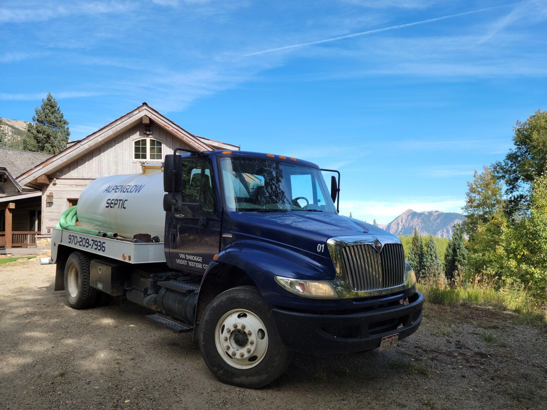 Dark blue and white utility truck parked beside a house on a gravel driveway with mountains in the background