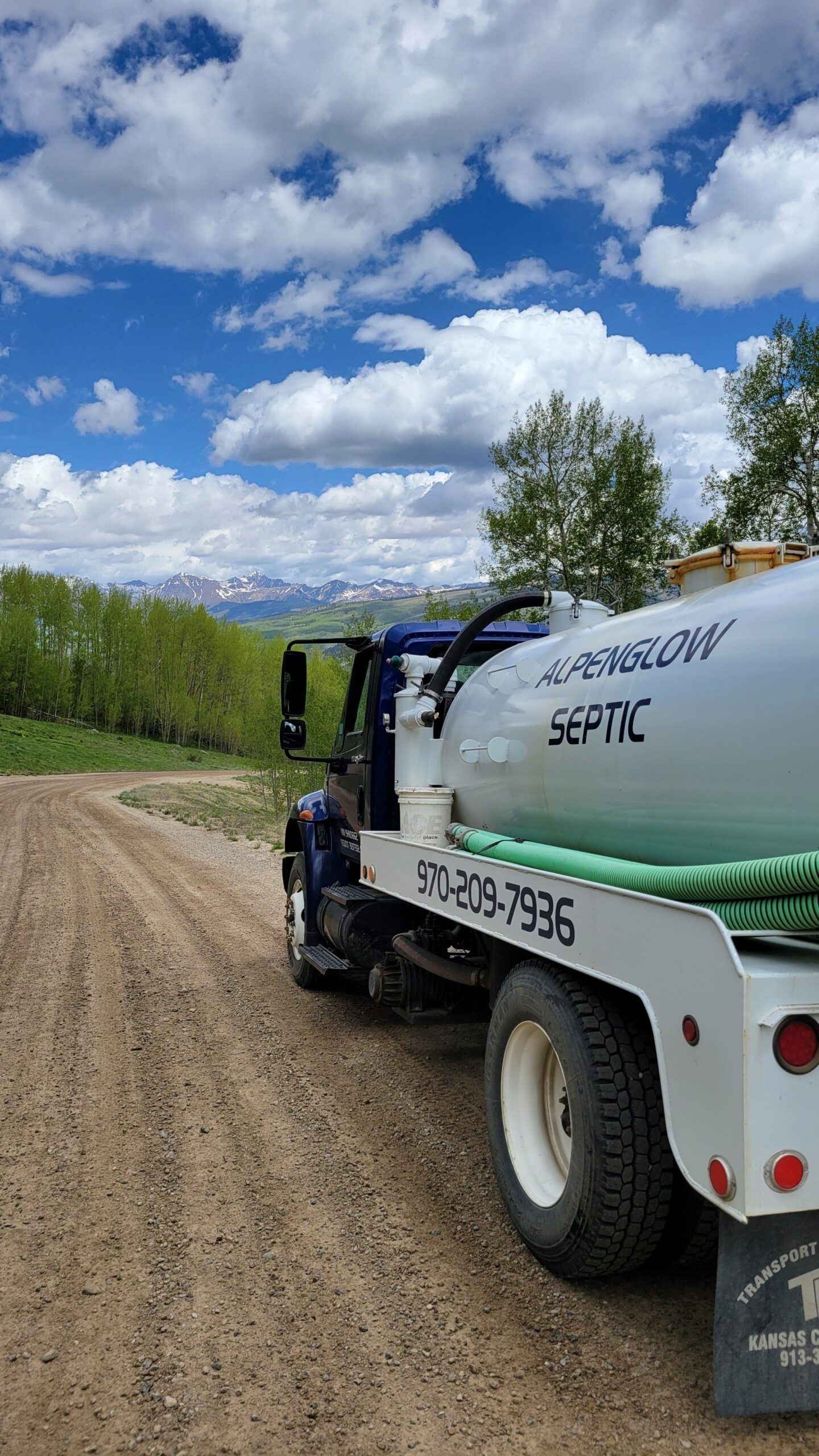 White water tanker truck on a gravel road beside green fields under a cloudy blue sky