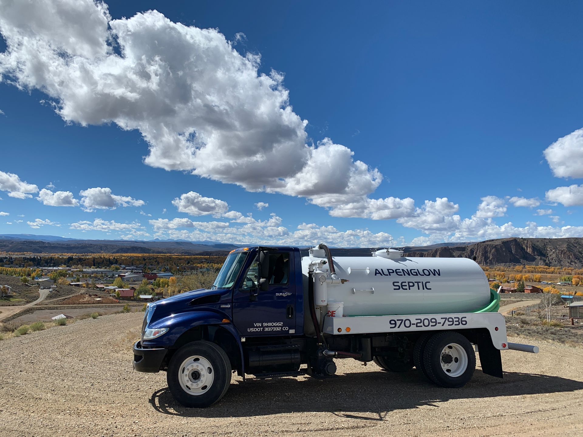 Blue utility truck parked on a dirt road under a cloudy sky in a rural landscape