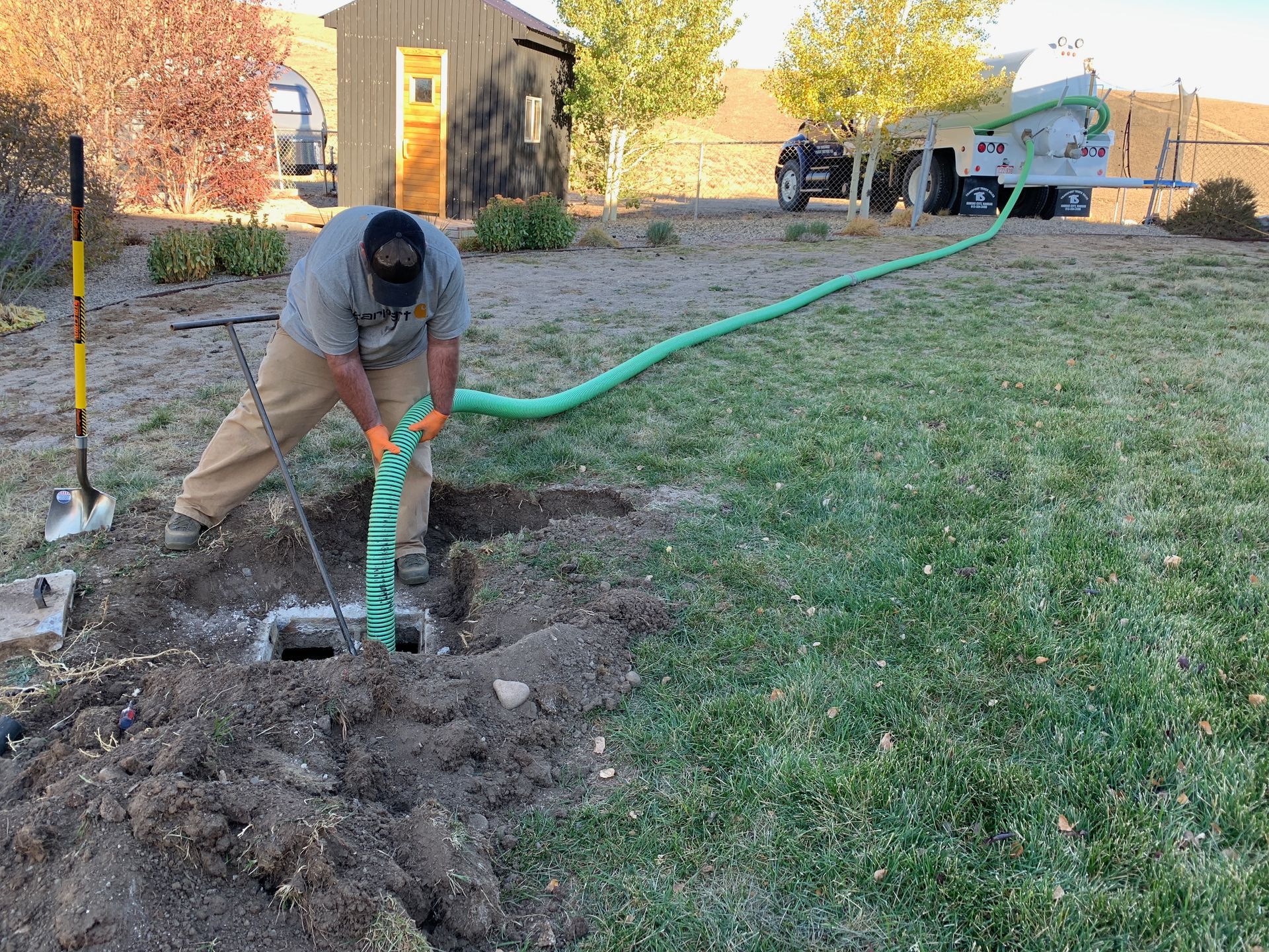 Worker using a green hose to backfill dirt in a yard near a house and truck