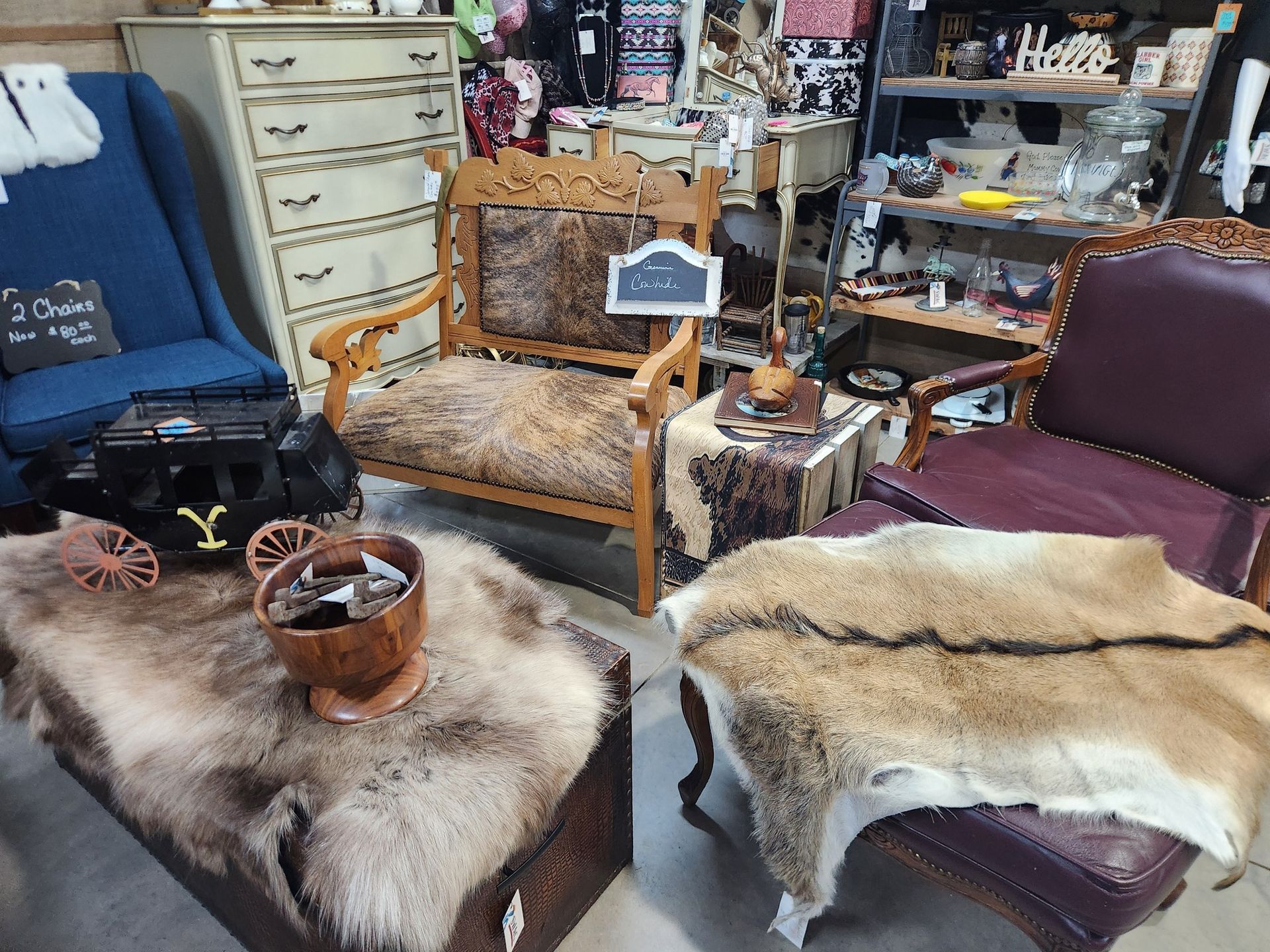 Vintage furniture in a shop, including chairs with animal hide coverings and a trunk, plus various decor.