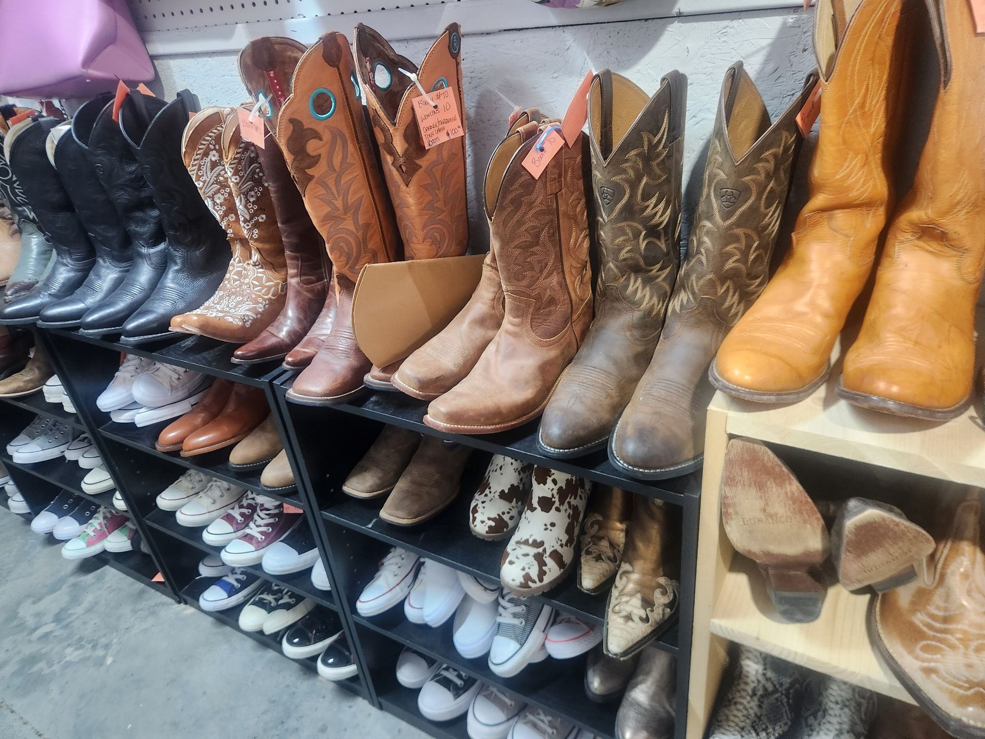 Rows of cowboy boots and sneakers displayed on shelves in a store.