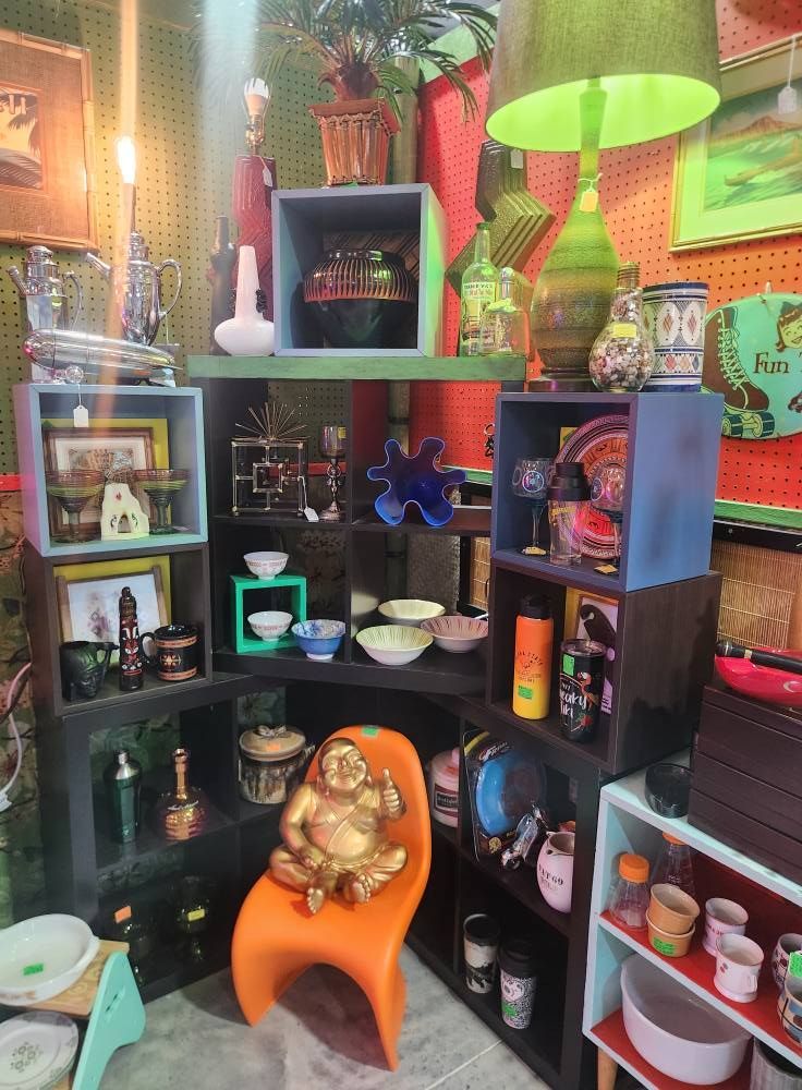 Display of vintage items on shelves in a shop, including lamps, figurines, dishes, and an orange chair.