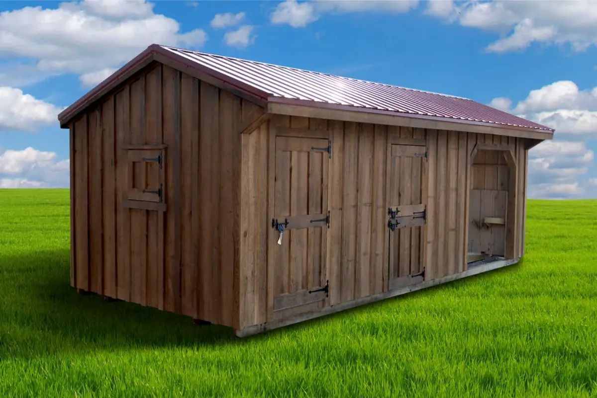 Wooden shed with a red roof, on a green field under a blue sky.