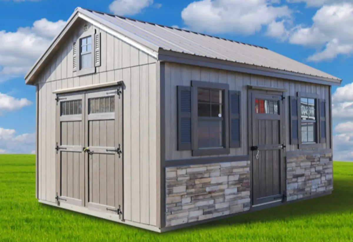 Gray shed with stone facade and gray trim, blue sky.