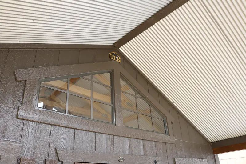 Triangular window in a brown shed, with light-colored, corrugated roof.