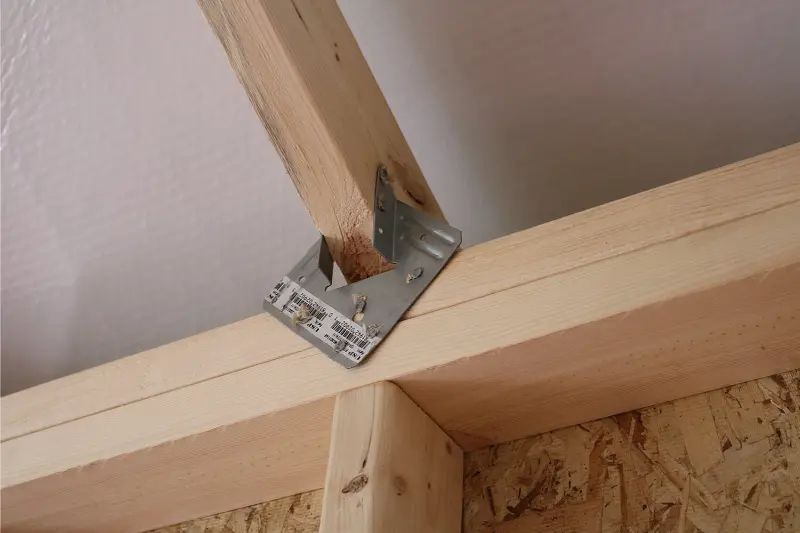 A wooden beam secured with a metal bracket to another beam inside a structure.