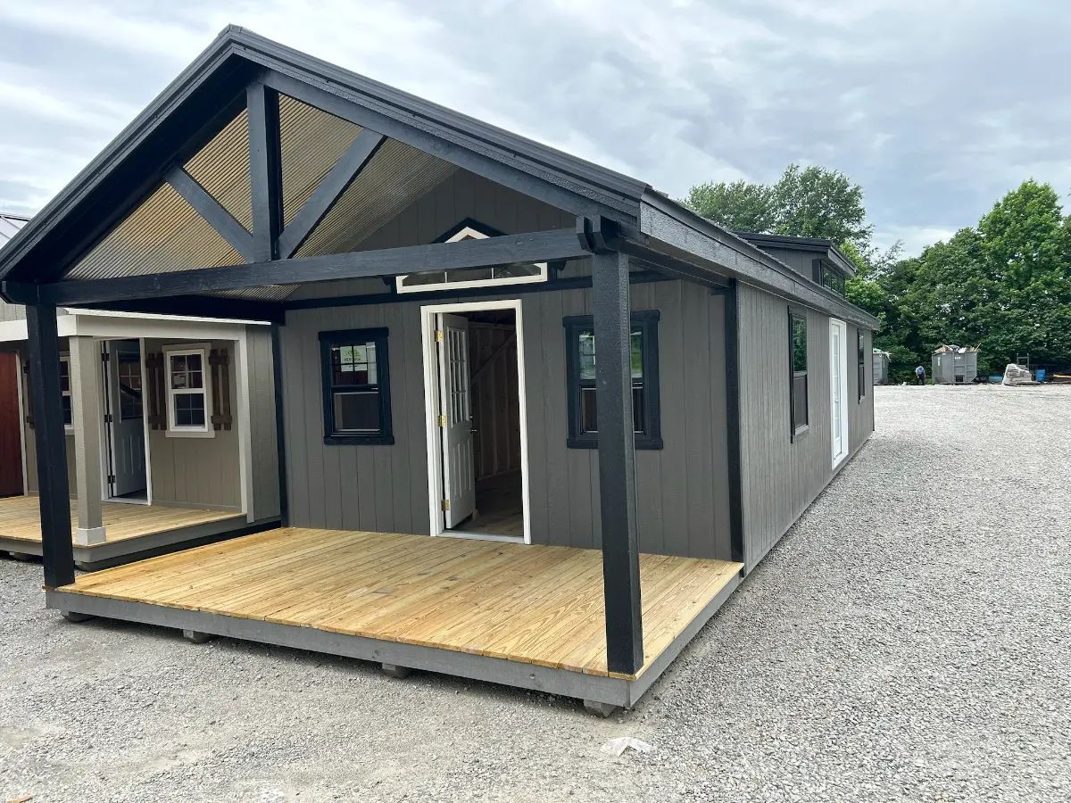 Gray tiny house with black trim, covered porch, and wooden deck.
