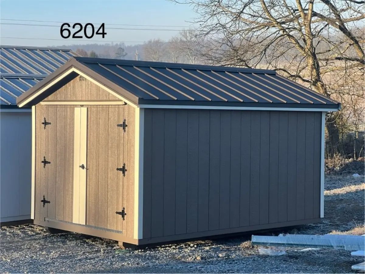 Gray storage shed with a metal roof, brown door, and off-white trim sits outdoors.