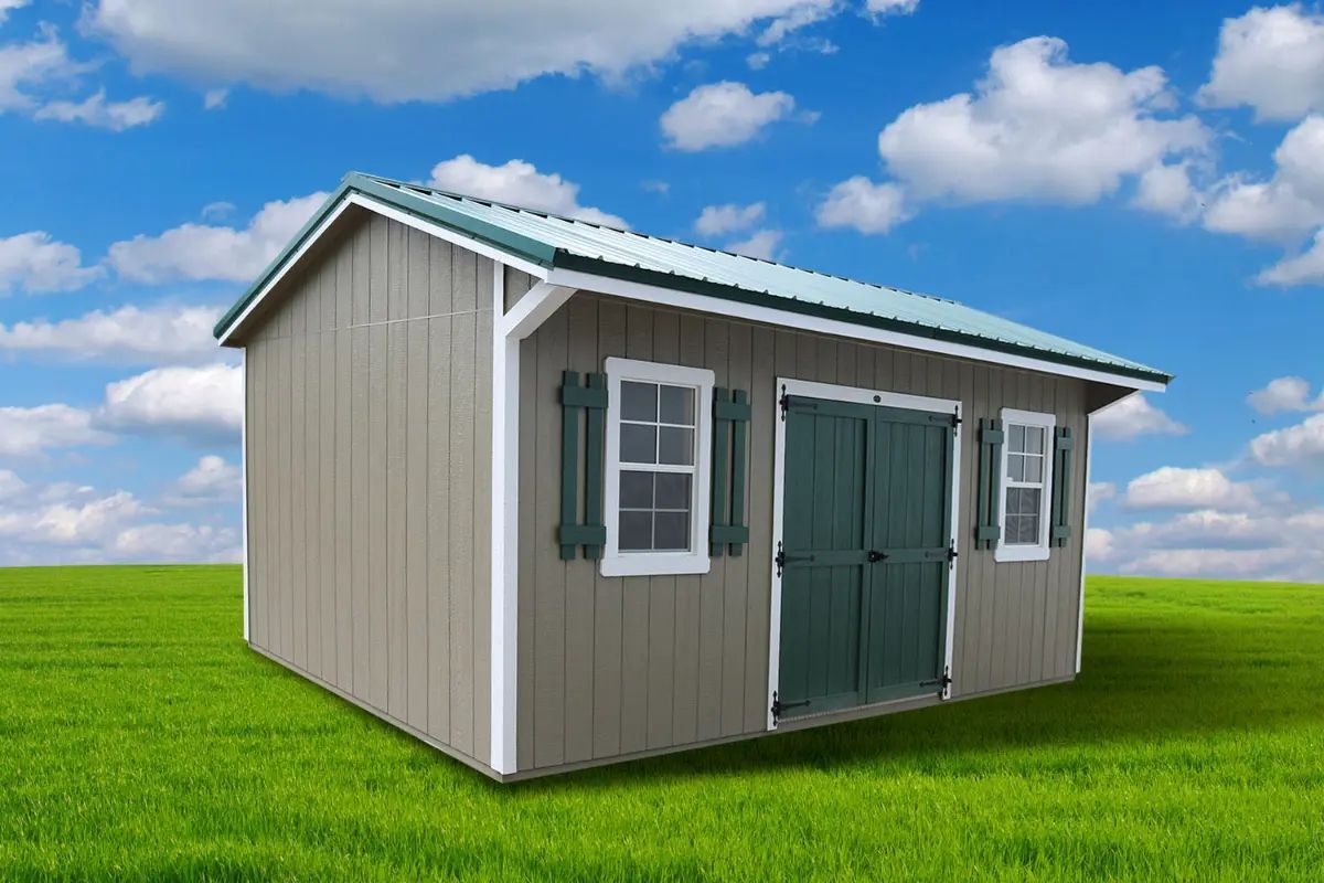 Tan shed with green roof and shutters on a grassy lawn under a blue sky with clouds.
