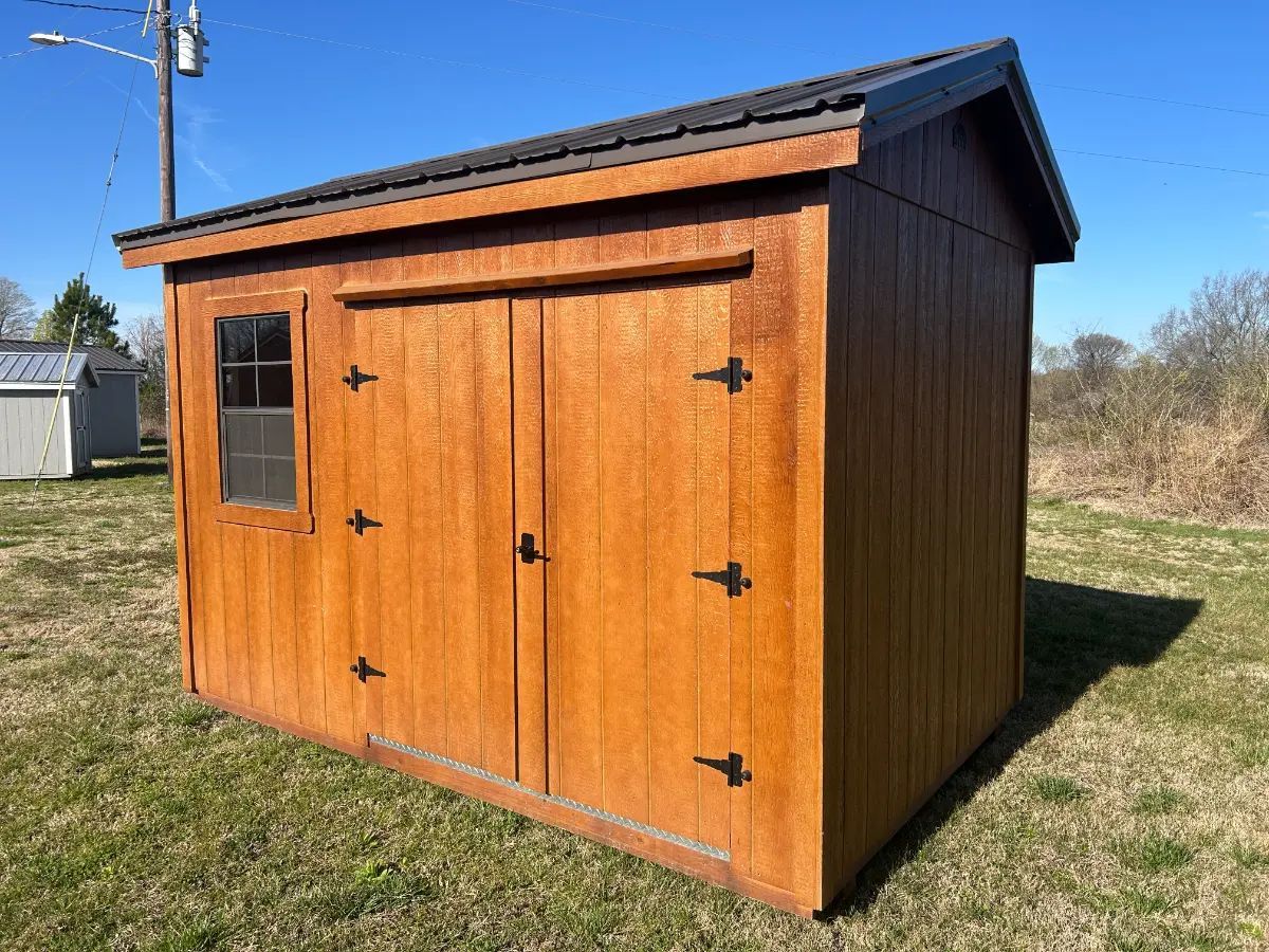Wooden shed with brown doors, window, and a black roof, set on grass.