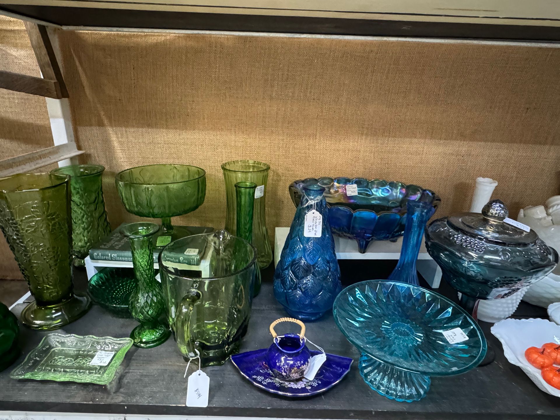 Display of various green and blue glass decorative items on a shelf, including vases and bowls.