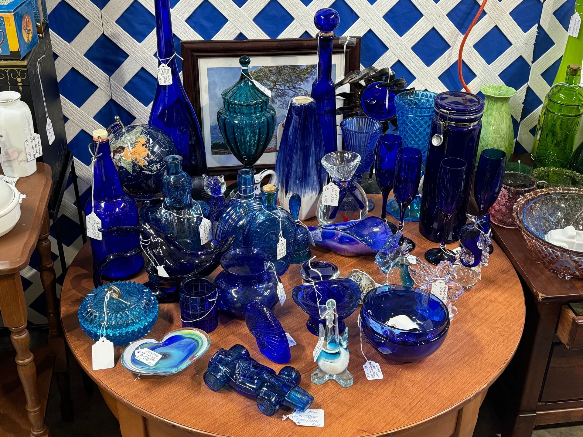 Display of antique cobalt blue glass objects on a round table, including bottles, bowls, and vases.