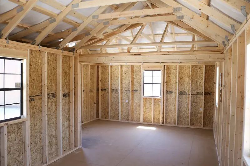 Interior of a wooden structure under construction; bare walls, windows, and roof framing are visible.