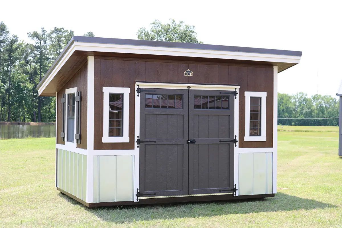 Brown and white shed with double doors and windows on grass.